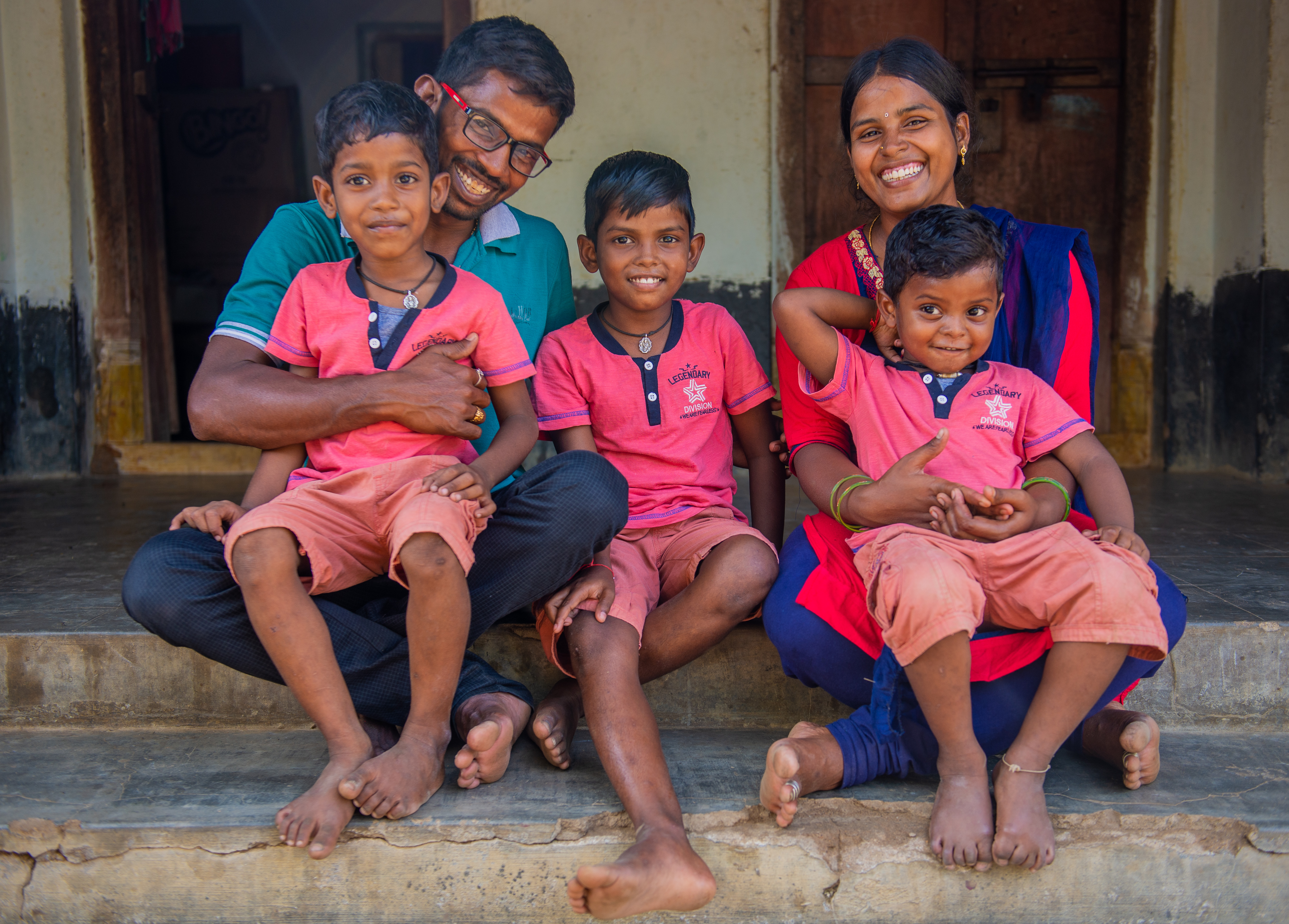 Anuradha sit on the steps outside her home in India, with husband Krishna and their three sons